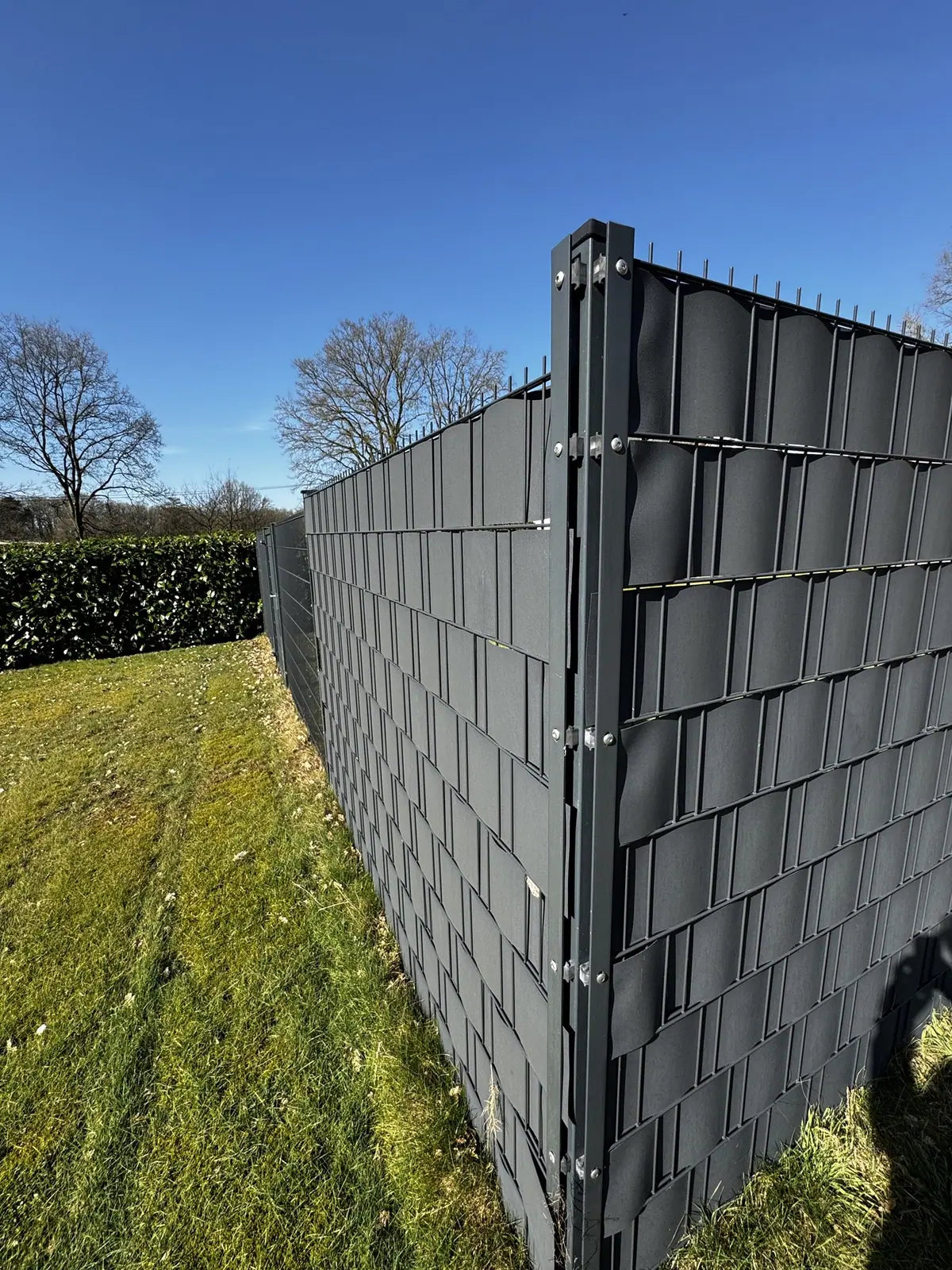 Zaunecke in Anthrazit mit eingeflochtenen Sichtschutzstreifen vor blauem Himmel